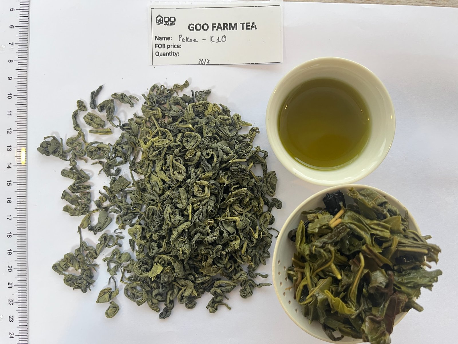 Feuilles de thé vert en vrac dans un bol blanc à côté d'une théière en verre remplie de thé vert